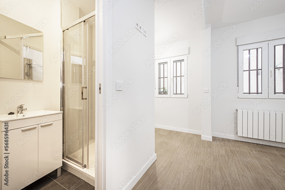 empty room with a pair of white aluminum windows with metal bars and access to a bathroom with white furniture and a shower cabin empty room with a pair of white aluminum windows with metal bars and access to a bathroom with white furniture and a shower cabin