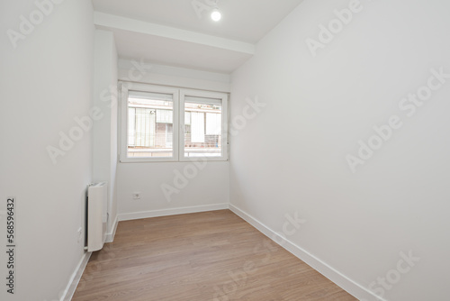 Small empty room with laminated flooring  double-paned white aluminum window and white aluminum radiator