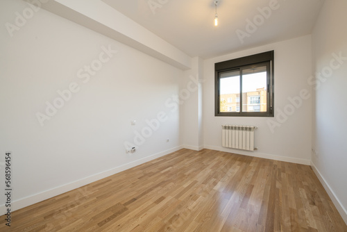 Empty room with plain white painted walls, dark aluminum windows with radiator below and floating oak flooring