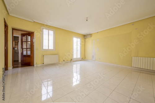 totally empty living room with light yellow painted walls  plaster molded ceilings and glossy white tile floors