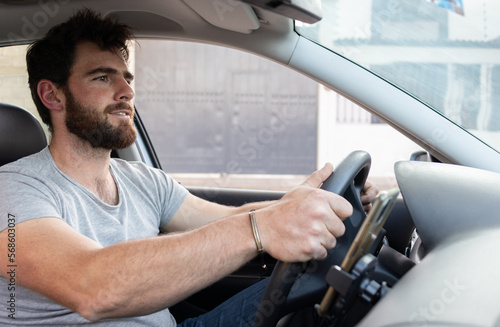young good looking bearded man driving a car, app driver holding the steering wheel using grey shirt