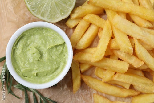 Delicious french fries, avocado dip, lime and rosemary on parchment, top view