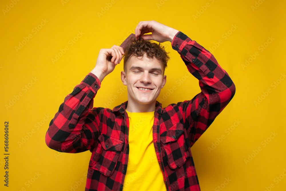 guy with a curly hairstyle combs his hair and smiles on a yellow background, a man takes care of his hair guy with a curly hairstyle combs his hair and smiles on a yellow background, a man takes care of his hair