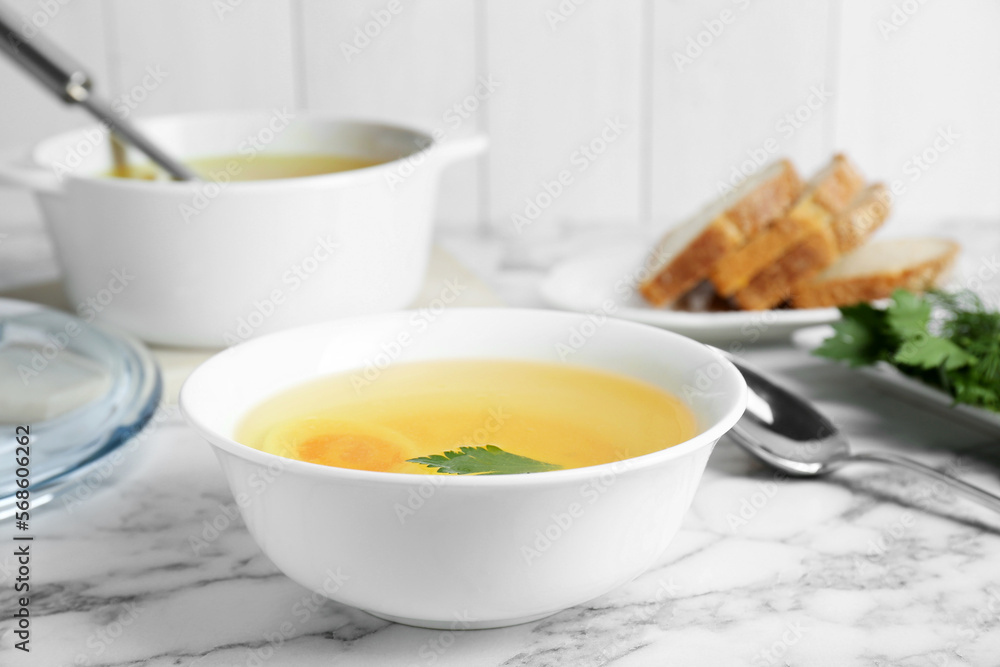 Delicious bouillon with egg and parsley in bowl on white marble table Delicious bouillon with egg and parsley in bowl on white marble table