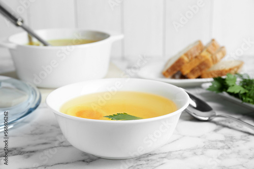 Delicious bouillon with egg and parsley in bowl on white marble table
