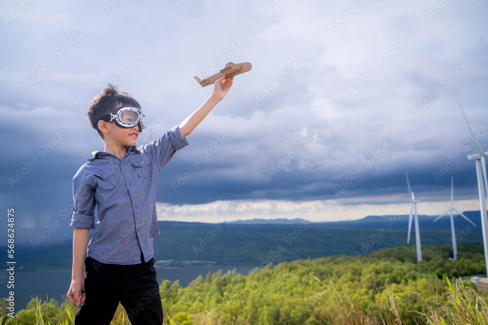 Happy Asian boy playing toy plane with wind turbine in the background.