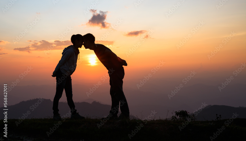 Silhouette of a couple on the mountain, A young romantic couple enjoy a beautiful view of the sun setting over the mountains, love, Valentine's Day.