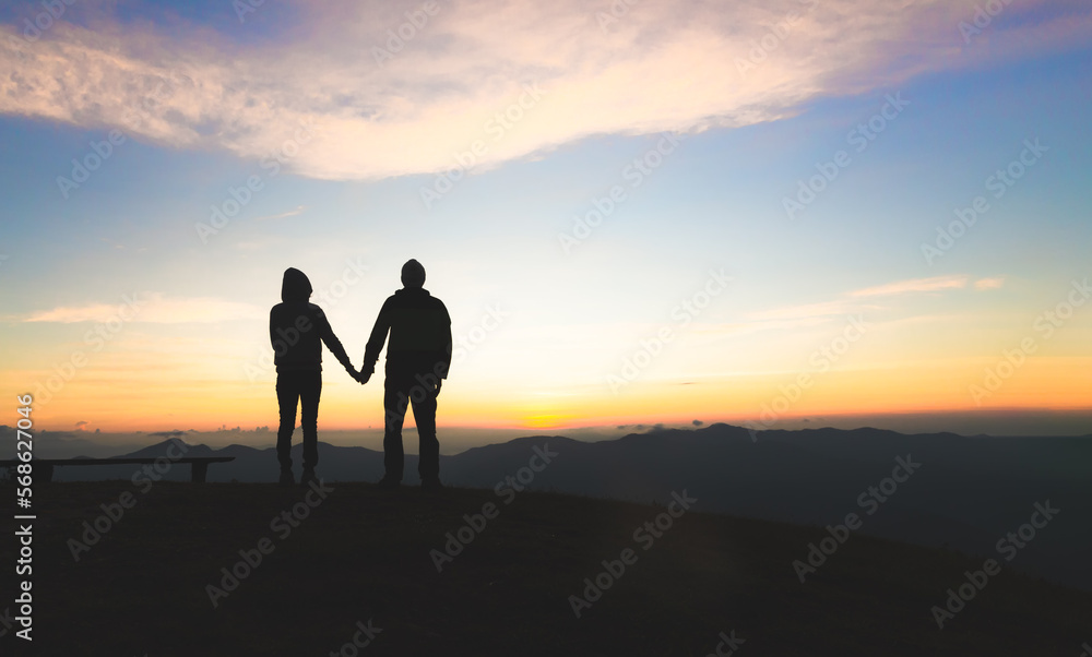 Silhouette of a couple on the mountain, A young romantic couple enjoy a beautiful view of the sun setting over the mountains, love, Valentine's Day.