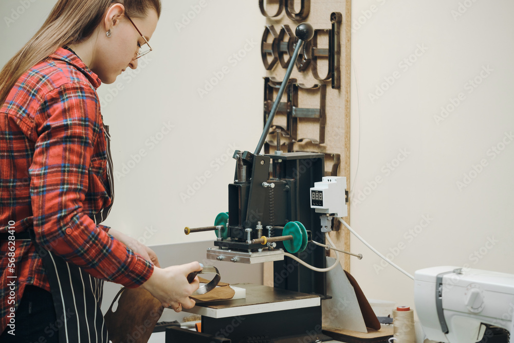 Woman sewing on professional sewing machine at her workplace. Tailor making accessories from eco leather. Handicraft concept. Female working in leather workshop