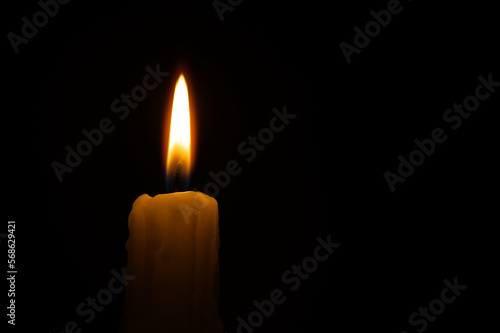 Single burning wax candle against a black background