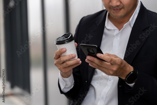 Close-up hand of Asian man holding a coffee cup and using a phone, Professionals Interacting With their devices in urban public spaces.