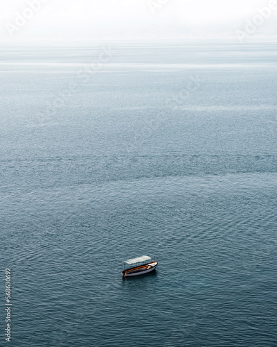 A small, forgotten boat sits idly on the calm surface of the vast and serene Ohrid lake, surrounded by breathtaking natural beauty. © Goran