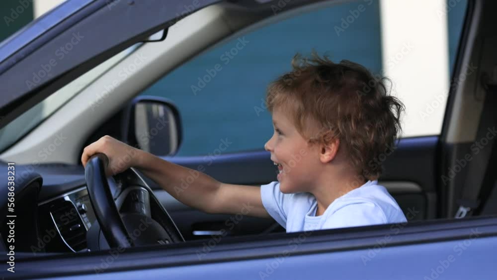 Little curly boy spins the steering wheel sitting in driver's seat, pretending to be racer. Child learns to drive a real car, playing in black interior of car Little curly boy spins the steering wheel sitting in driver's seat, pretending to be racer. Child learns to drive a real car, playing in black interior of car