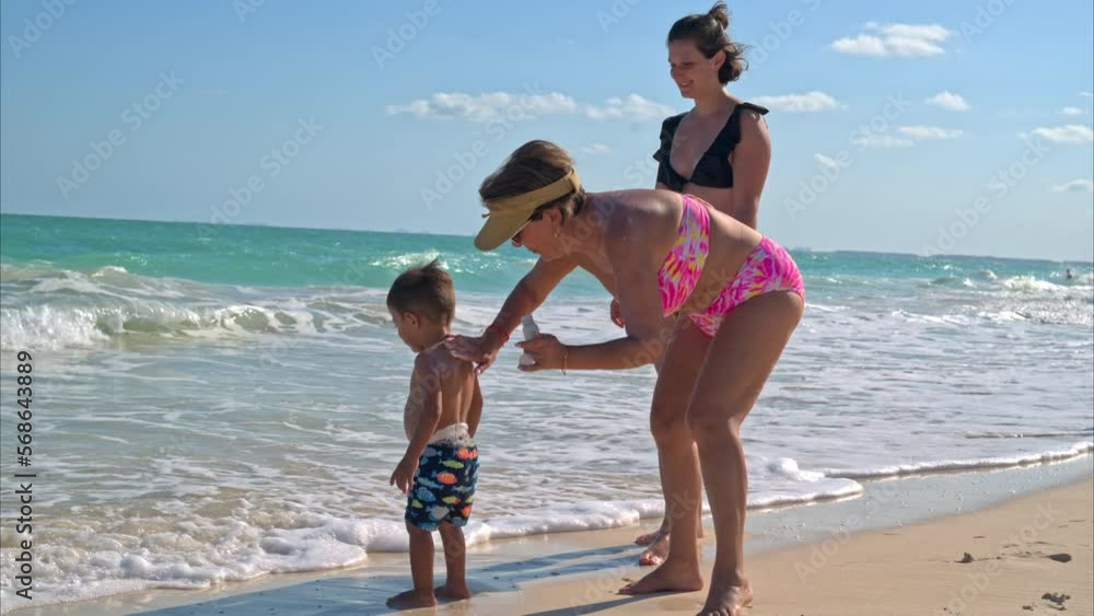 Slow motion of a senior latin woman spreading sunscreen on her grandson to protect him from the sun on a warm tropical day Slow motion of a senior latin woman spreading sunscreen on her grandson to protect him from the sun on a warm tropical day