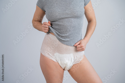 Woman in adult diapers and gray t-shirt on a white background. Incontinence problem.