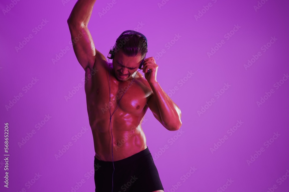 Man wearing headphones athletic physique bodybuilder nude torso abs full-length, fitness classes, purple colored light. Advertising, sports, active lifestyle, competition, challenge concept. Man wearing headphones athletic physique bodybuilder nude torso abs full-length, fitness classes, purple colored light. Advertising, sports, active lifestyle, competition, challenge concept.