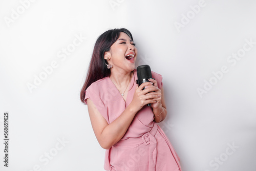 Portrait of carefree Asian woman, having fun karaoke, singing in microphone while standing over white background