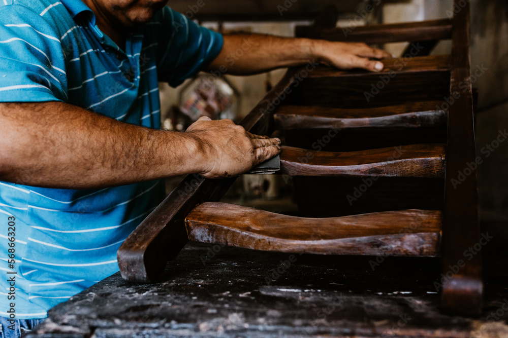 hispanic senior man carpenter working working on a wood chair at the furniture workshop in Mexico Latin America