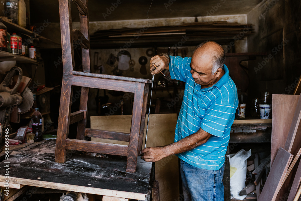 hispanic senior man carpenter working working on a wood chair at the furniture workshop in Mexico Latin America hispanic senior man carpenter working working on a wood chair at the furniture workshop in Mexico Latin America