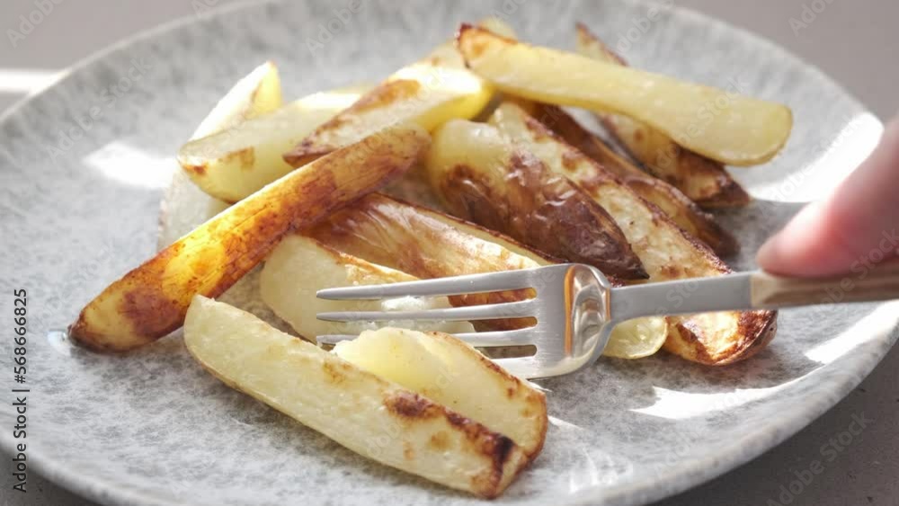 Hand eating slices of hot crispy baked potato with a fork on a gray plate. Hand eating slices of hot crispy baked potato with a fork on a gray plate.