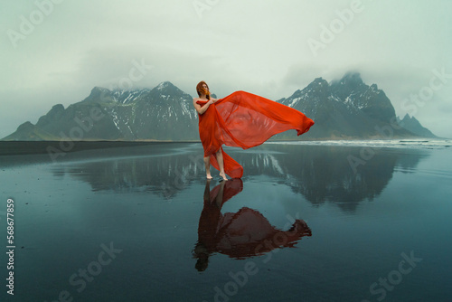 Sensual woman in red clothes on Reynisfjara beach scenic photography. Picture of person with hills on background. High quality wallpaper. Photo concept for ads, travel blog, magazine, article