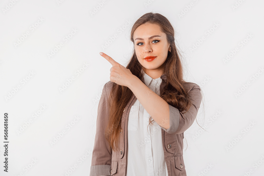 Confident young woman points finger left, showing news, promo banner, offer. Beautiful girl in casual clothes, looks serious, stands against neutral studio background Confident young woman points finger left, showing news, promo banner, offer. Beautiful girl in casual clothes, looks serious, stands against neutral studio background