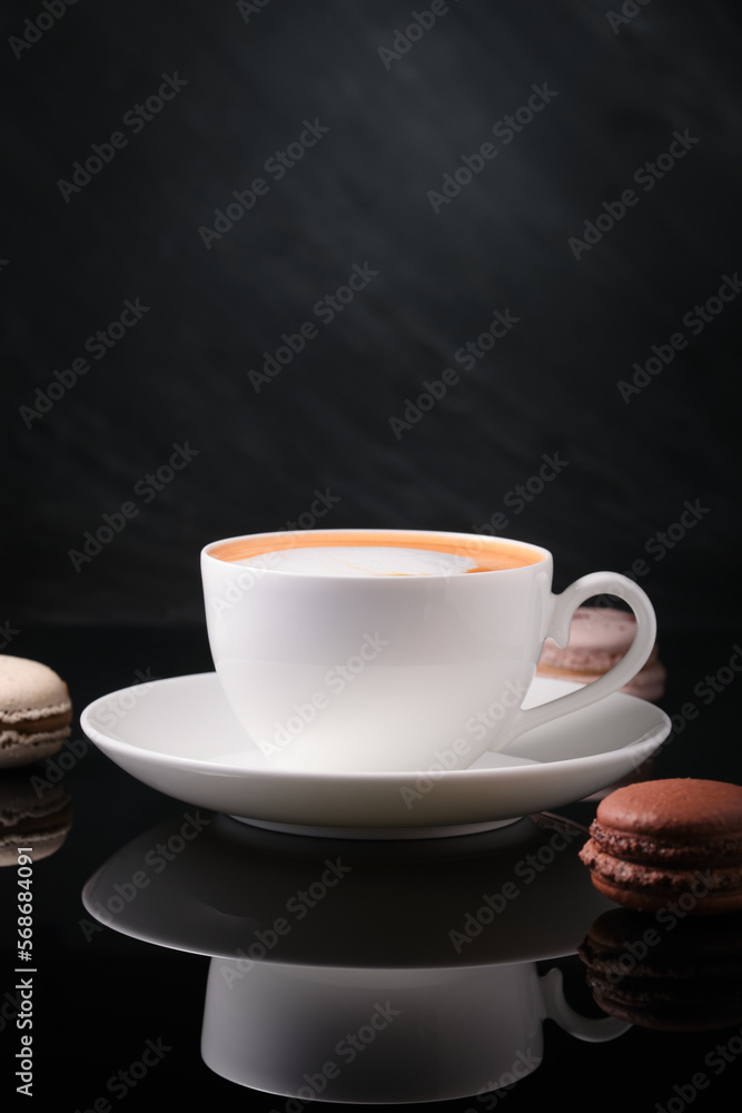 White cup with cappuccino on a dark background, reflection of a mirror table. breakfast on a black background. Coffee with macaroon on a black background. White cup with cappuccino on a dark background, reflection of a mirror table. breakfast on a black background. Coffee with macaroon on a black background.