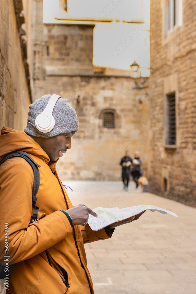 Young man on vacation with winter clothes, headphones and map visiting the gothic quarter of Barcelona (Spain).