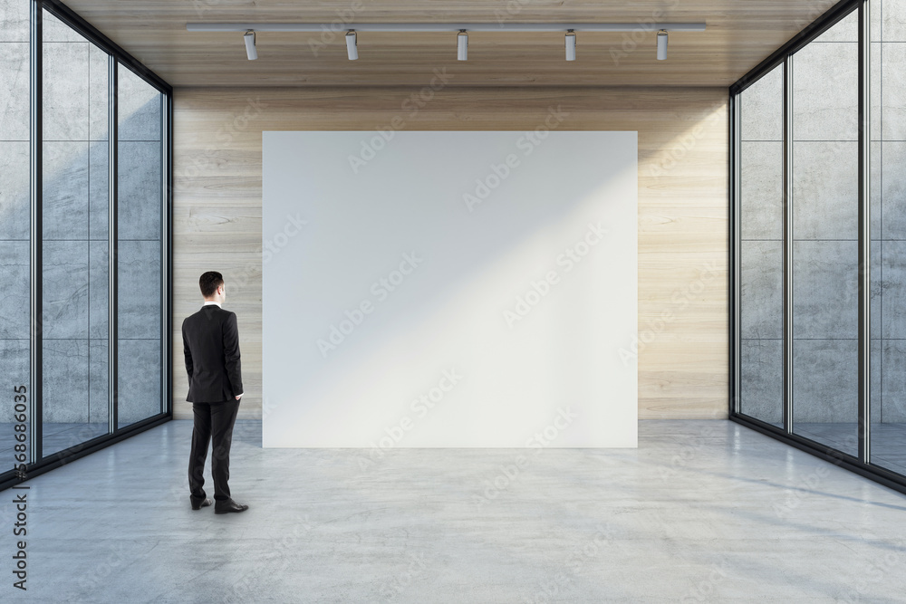 Man in black suit back view looking at blank white partition with place for your logo or advertising text on light wooden background in empty hall with transparent walls and concrete floor, mock up Man in black suit back view looking at blank white partition with place for your logo or advertising text on light wooden background in empty hall with transparent walls and concrete floor, mock up