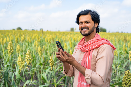 Farmer with mobile phone at agricultural farm land looking at camera showing with copy space - concept of technology, banking or financial and modern village farmer