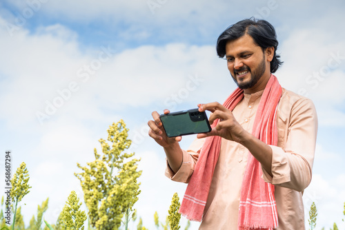Canvas Print Happy young farmer checking crop growth by taking photos on mobile phone app at
