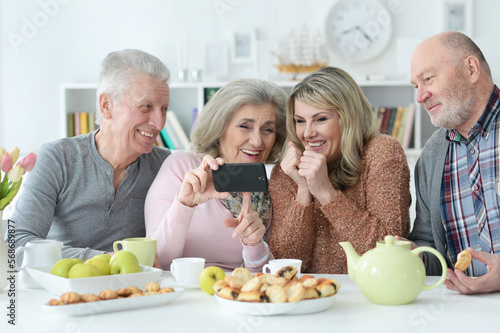 two Senior couples using smartphone during morning tea