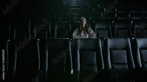 A young woman is sitting alone in the cinema and watching a movie. Evening of entertainment