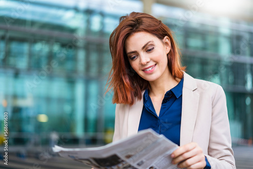 Smiling redheaded businesswoman reading newspaper photo