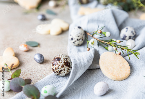 Easter cookies with candies shaped eggs, floral decor and quail eggs on linen napkin on stone background. Holiday concept.