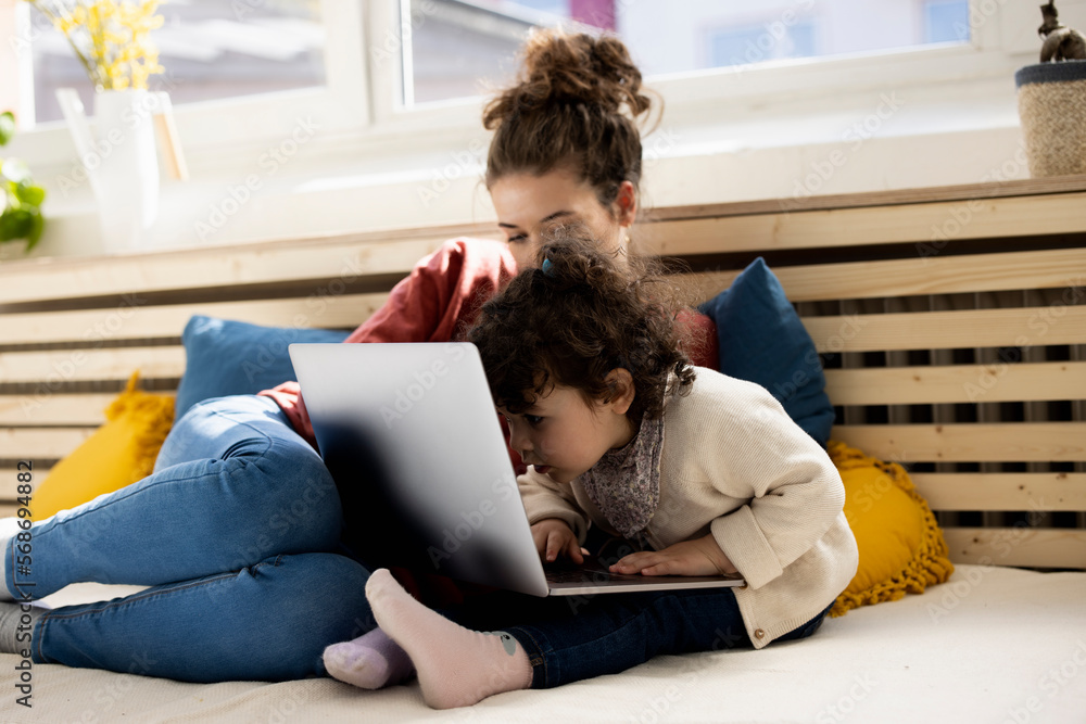 Little girl using laptop sitting on lap of mother on couch at home Little girl using laptop sitting on lap of mother on couch at home