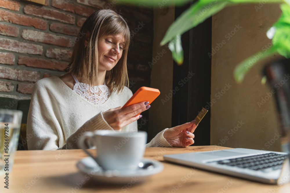 Smiling freelancer with credit card using smart phone at cafe Smiling freelancer with credit card using smart phone at cafe
