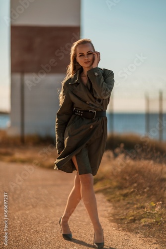 Portrait blonde sea cape. A calm young blonde in a khaki raincoat stands on the seashore against the backdrop of a lighthouse. © svetograph
