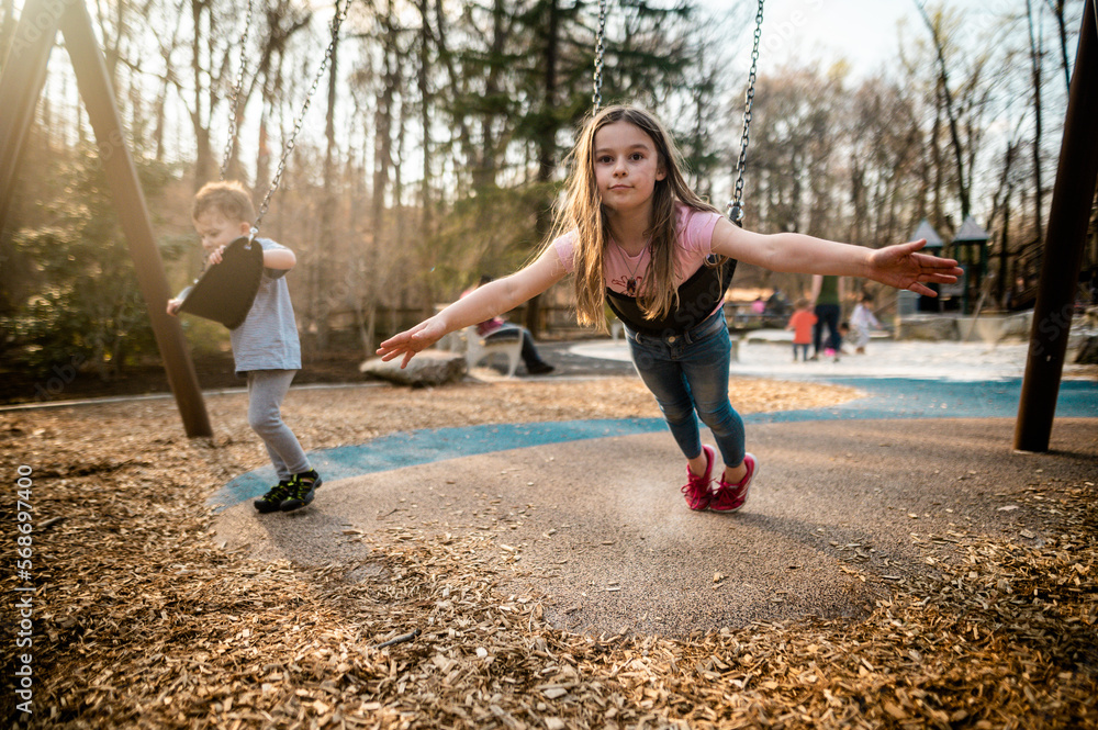 Brother and sister play on the swings at playground at sunset Stock ...
