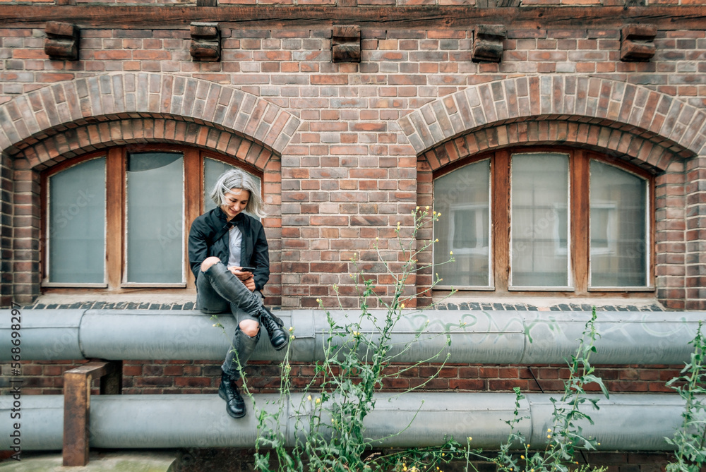 Woman sits on pipe near abandoned building, looks at smartphone Woman sits on pipe near abandoned building, looks at smartphone