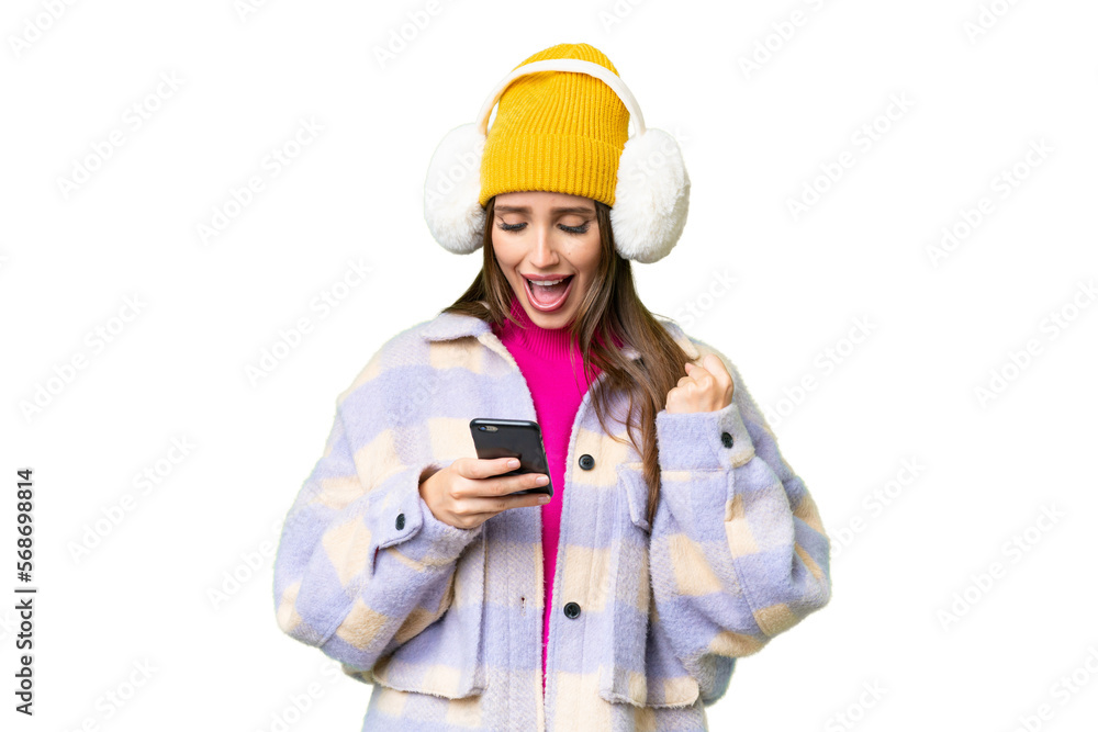 Young woman wearing winter muffs over isolated chroma key background surprised and sending a message Young woman wearing winter muffs over isolated chroma key background surprised and sending a message