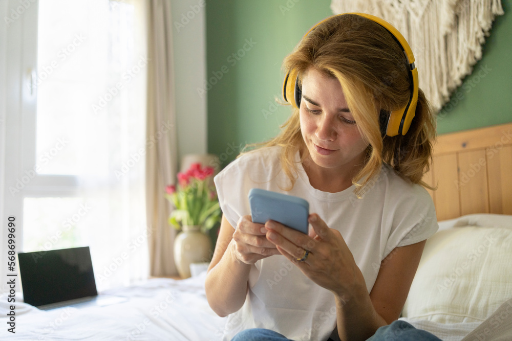 Smiling woman wearing wireless headphones using smart phone Smiling woman wearing wireless headphones using smart phone