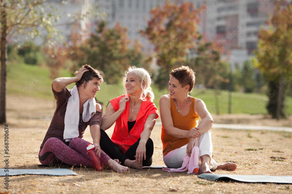 Active elderly women on fitness training in public park, relaxing and talking after workout. Happy Mature female friends outdoors