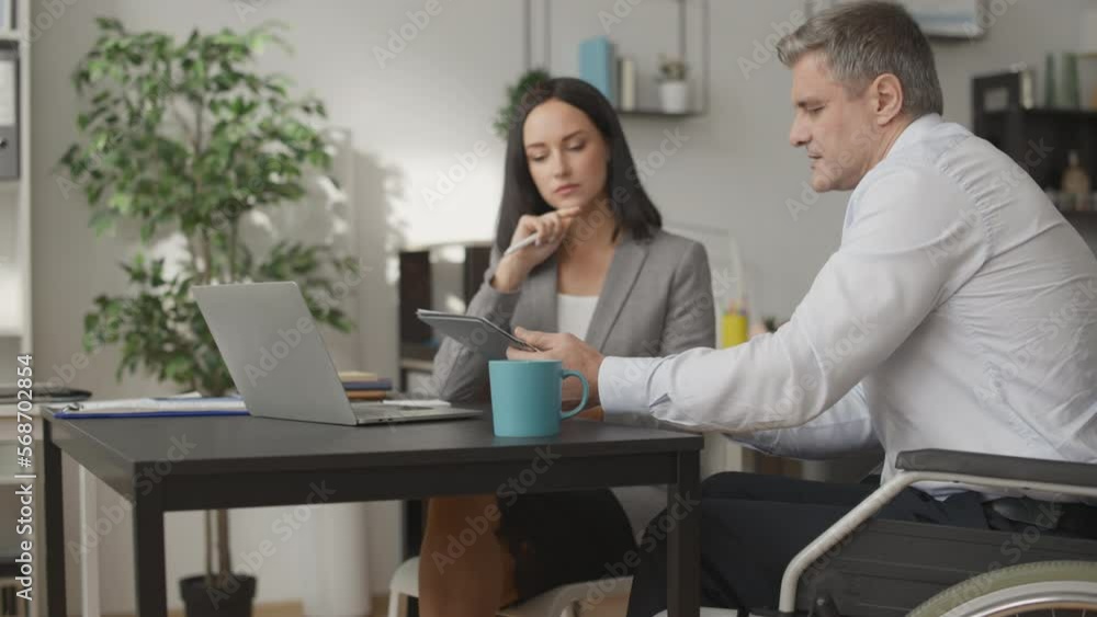 Male company employee with disability working on project together with colleague Male company employee with disability working on project together with colleague