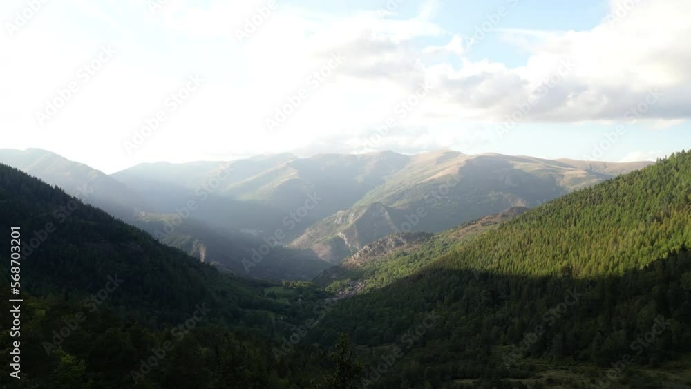 DRONE SHOT: Slow pan over mountain range with a tree in front and sun rays shining over mountains. Sun shines on the mountain on the other side DRONE SHOT: Slow pan over mountain range with a tree in front and sun rays shining over mountains. Sun shines on the mountain on the other side