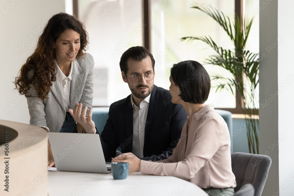 Diverse team of millennial colleagues talking at office laptop, brainstorming on new ideas, working on online project strategy, plan, issues together, discussing tasks, teamwork