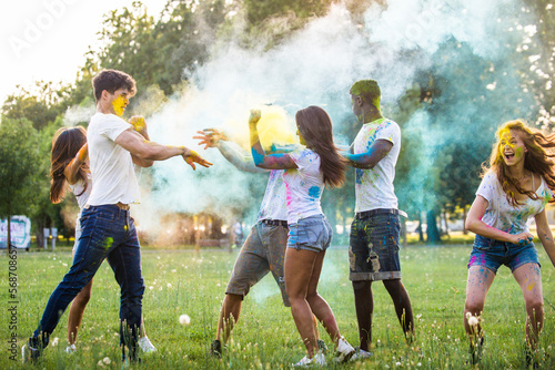 Multiethnic group of happy playful friends playing and having fun with holi colorful powder at the park