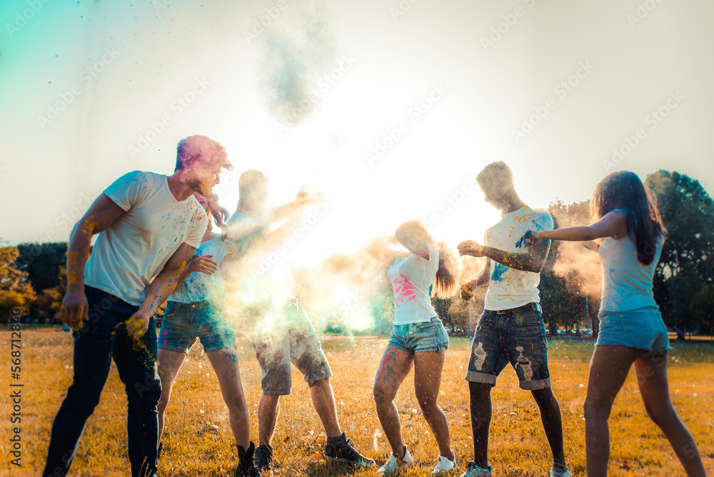 Obraz premium Multiethnic group of happy playful friends playing and having fun with holi colorful powder at the park