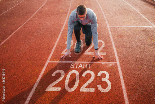 Start of new year 2023 symbol. Front view of a man preparing to run on athletics track engraved with the year 2023. Getting ready for the new year, success goal