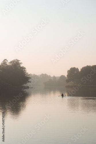A person is kayaking or canoe in the morning in lake surrounded by silhouette of trees